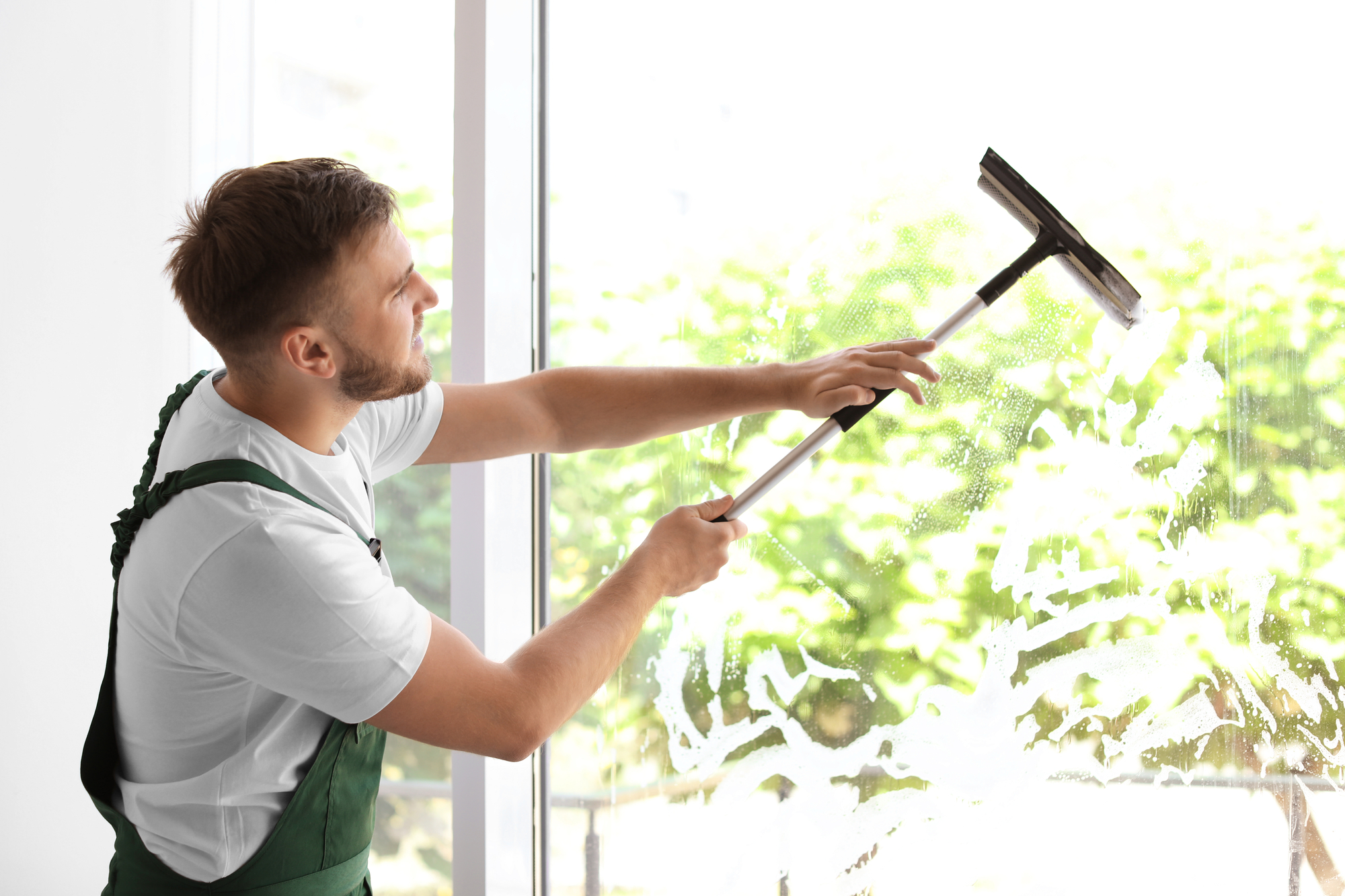 Man in Overalls Cleaning Window With Mop.